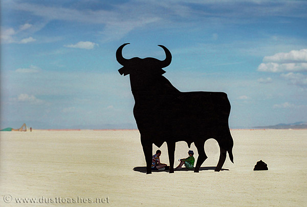 People sitting in the shadow of the bull art installation