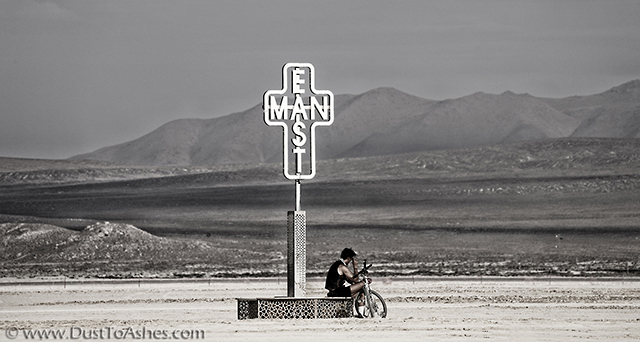 Lost man sitting next the sign in deep playa which reads East Man